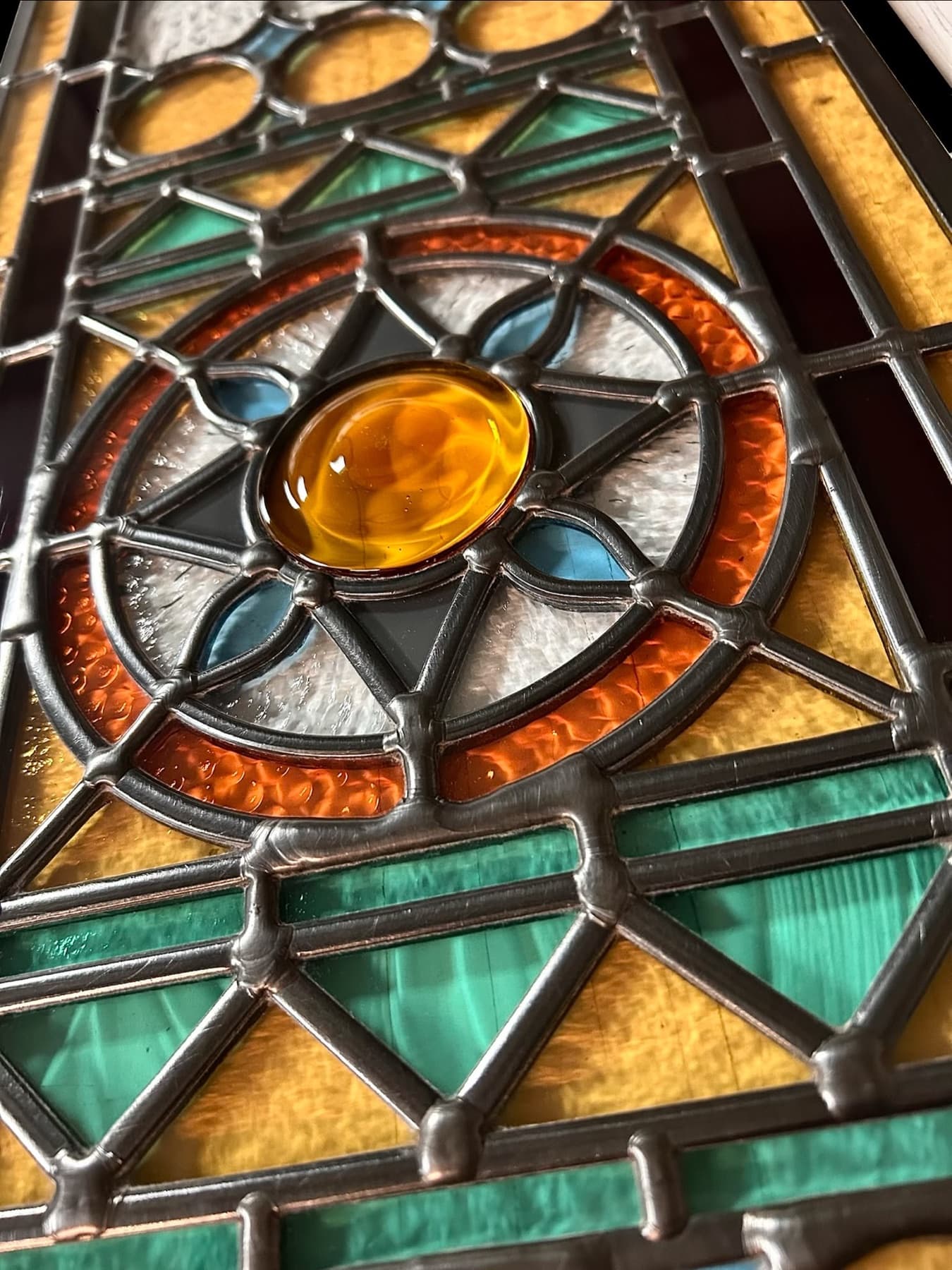 Close-up of a leaded panel with an amber roundel, copper-red ring and turquoise borders
